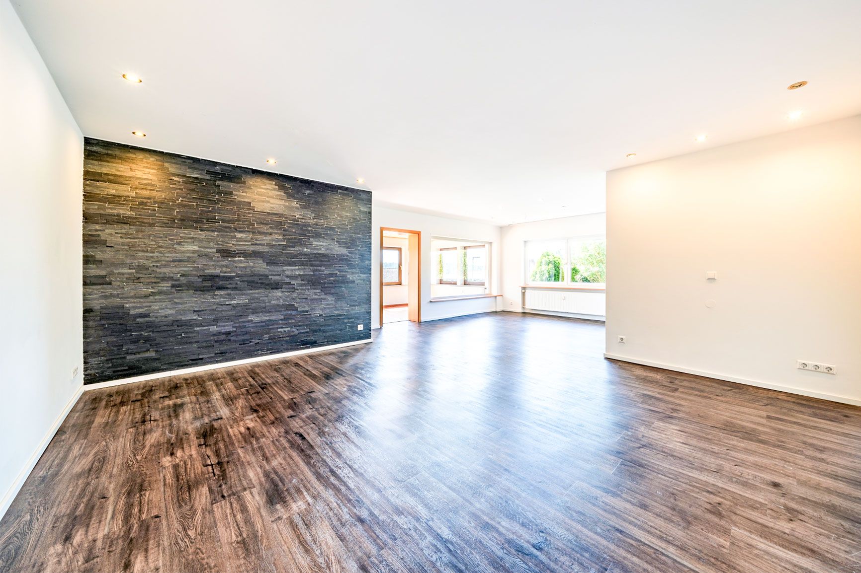 Helles Wohnzimmer mit dunklem Holzboden, Steinwand und großen Fenstern.