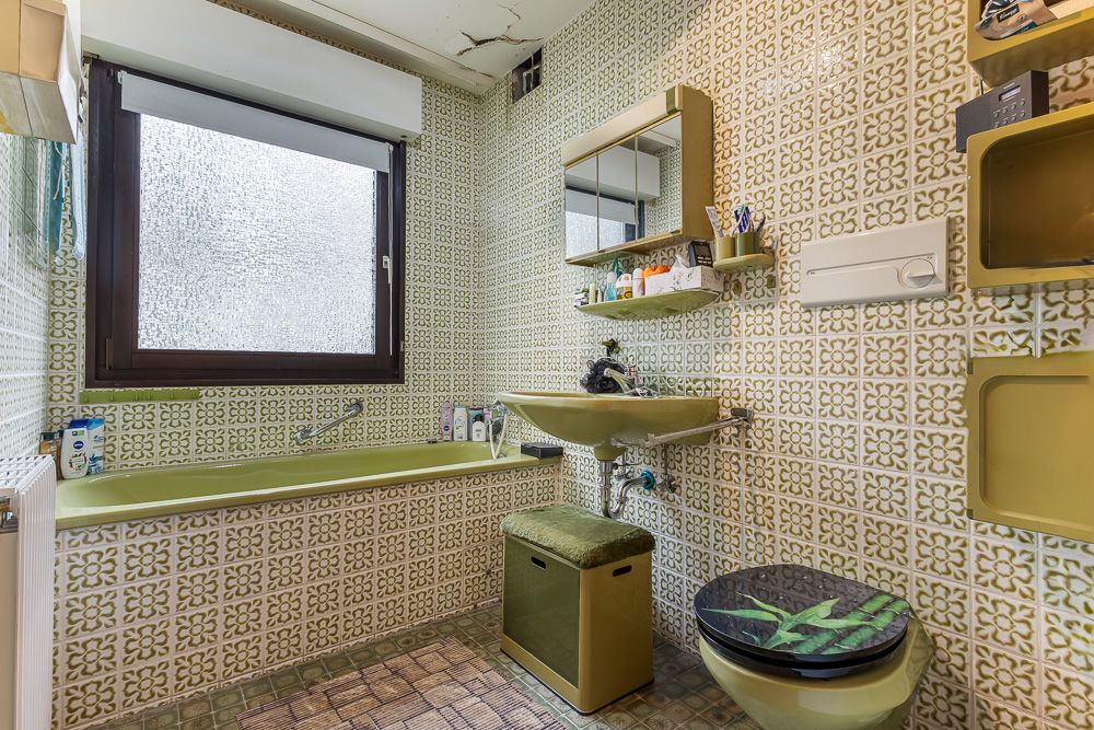 Badezimmer mit grüner Badewanne, grünem Waschbecken und gemusterten Fliesen an Wand und Boden.