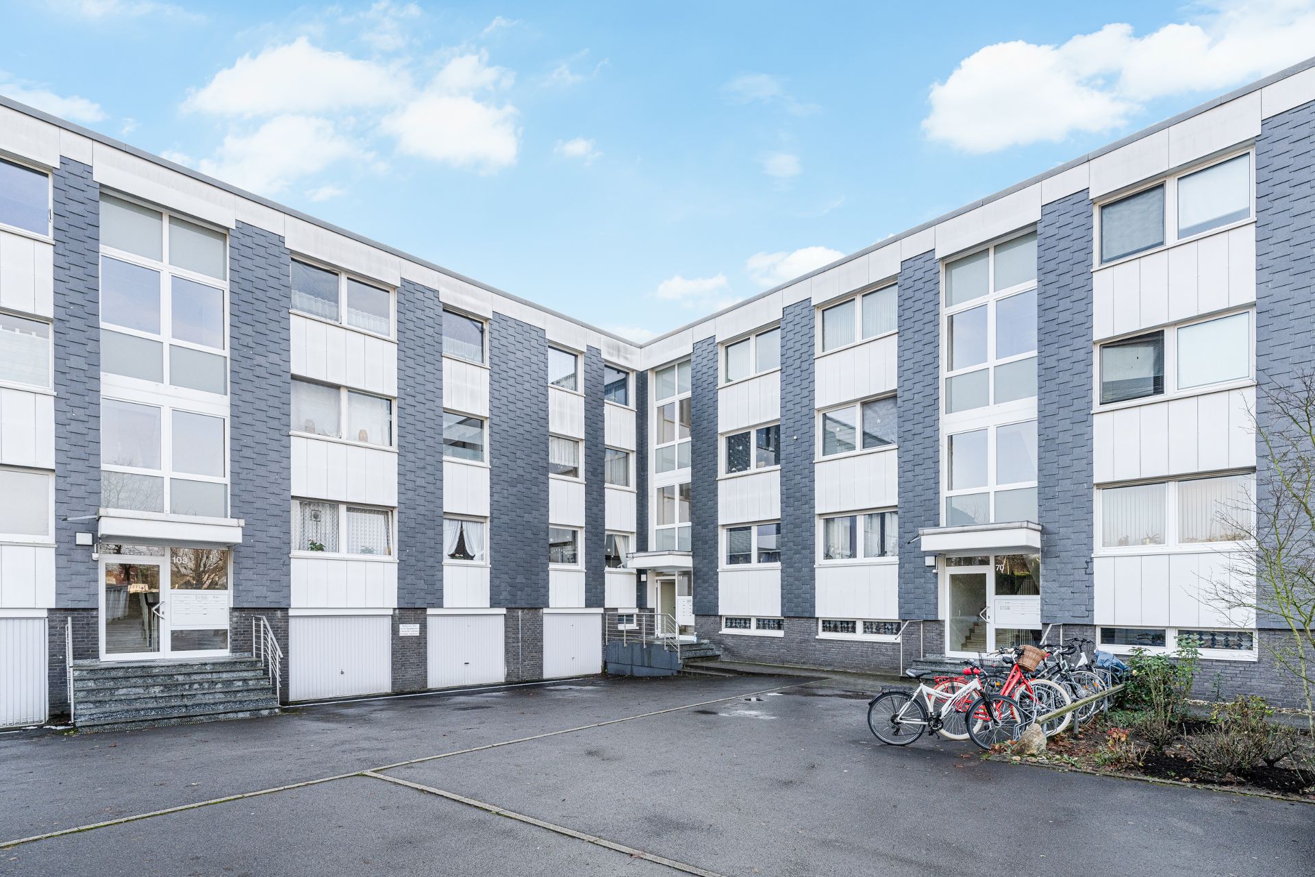 Dreistöckiges Wohnhaus mit großen Fenstern, Eingängen und Fahrrädern vor dem Gebäude.