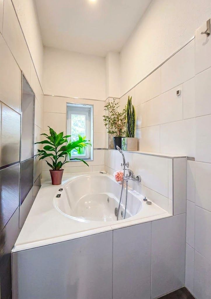 Helles Badezimmer mit großer Eckbadewanne, Zimmerpflanzen und kleinem Fenster.