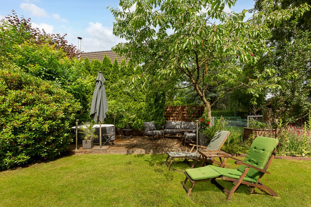 Garten mit Rasenfläche, Sitzgelegenheiten, Sonnenschirm und Bäumen.