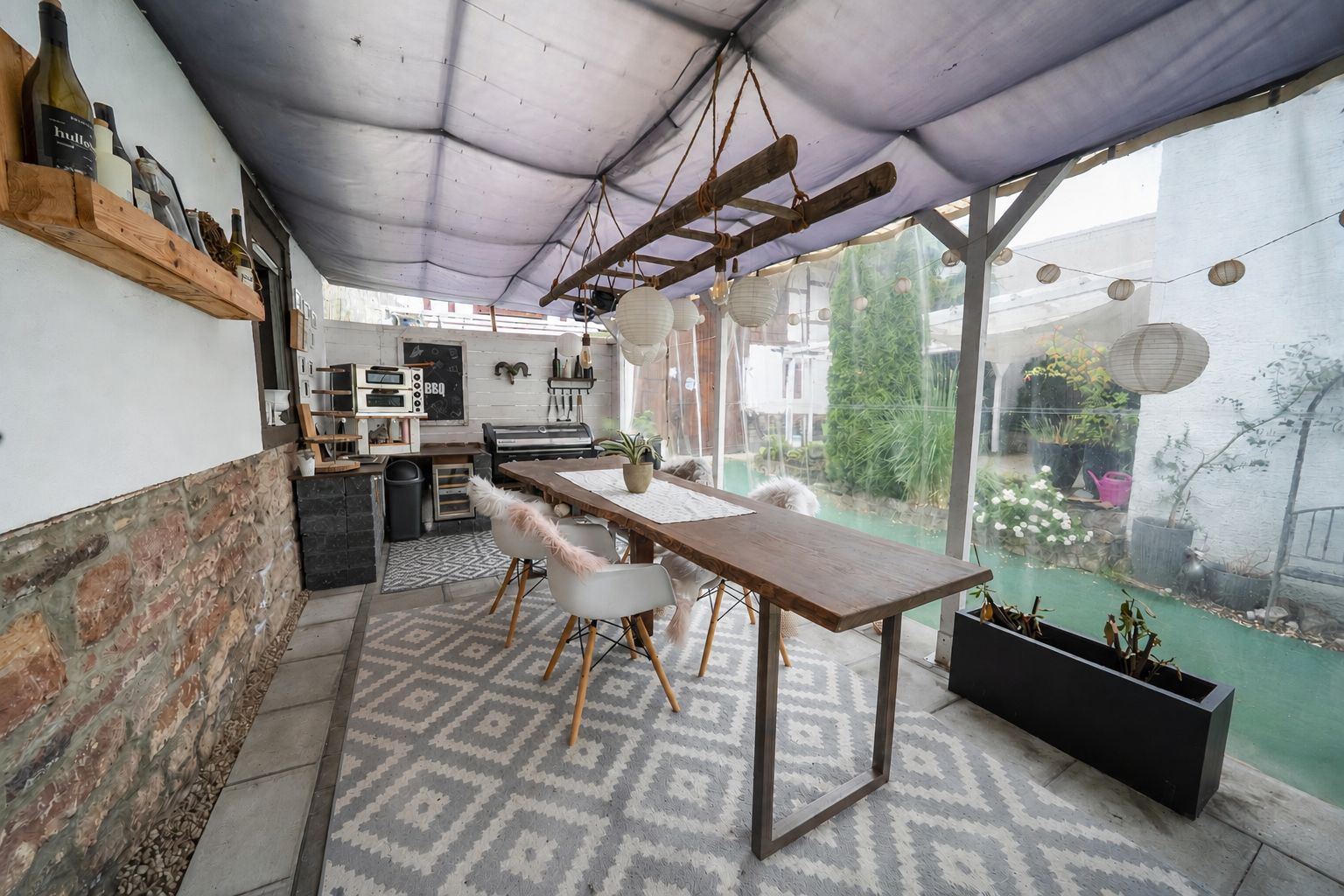 Überdachte Terrasse mit Esstisch, Stühlen und Hängelampen, Blick auf den Garten.