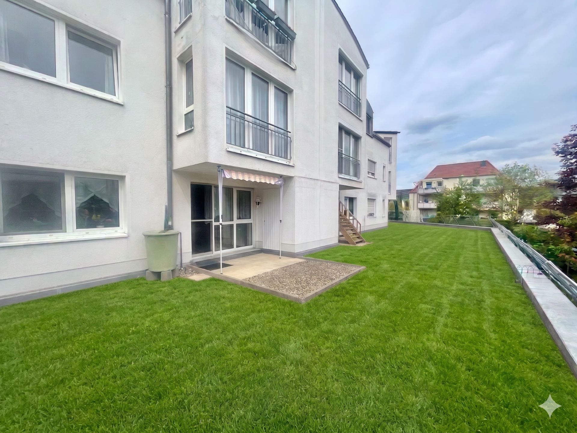 Weiße Wohngebäude mit großen Fenstern und Terrasse, umgeben von einer grünen Rasenfläche.