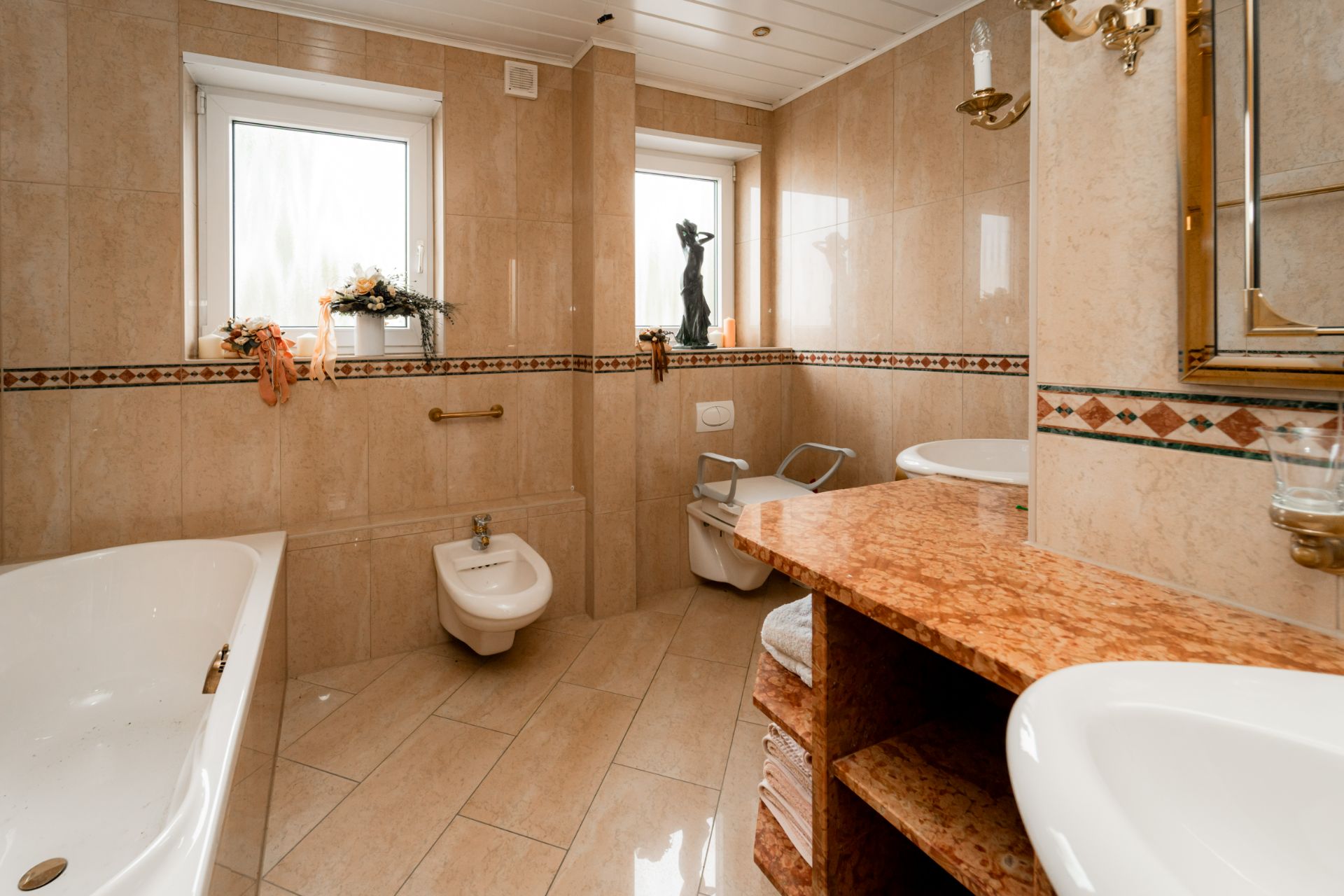 Modernes Badezimmer mit Badewanne, Bidet, WC, Doppelwaschbecken und zwei Fenstern.