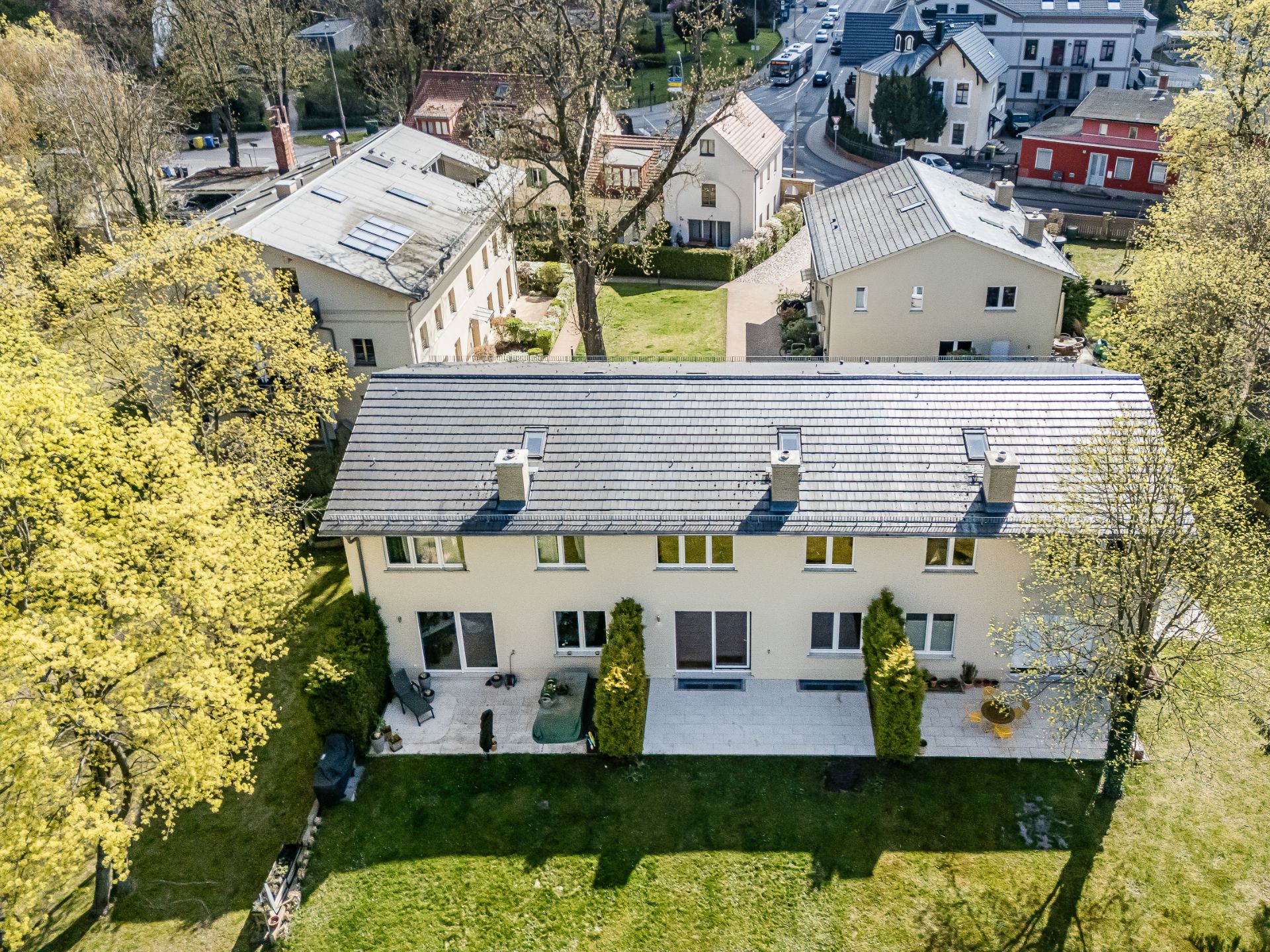 Drohnenaufnahme eines Reihenhauses mit Terrasse und grünem Garten, umgeben von Bäumen.