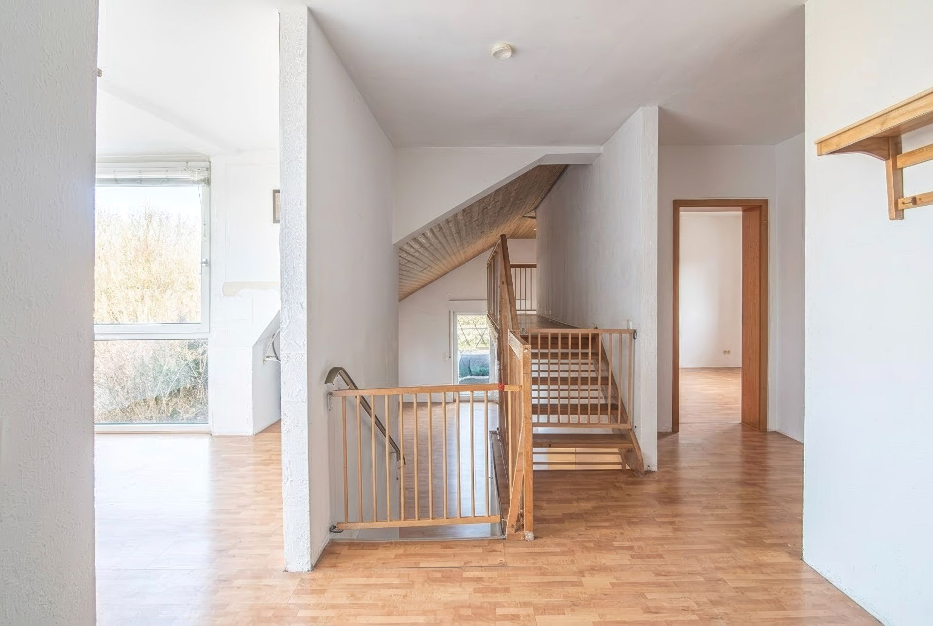Heller Flur mit Holztreppe, Holzboden und großen Fenstern, Türen zu weiteren Räumen.