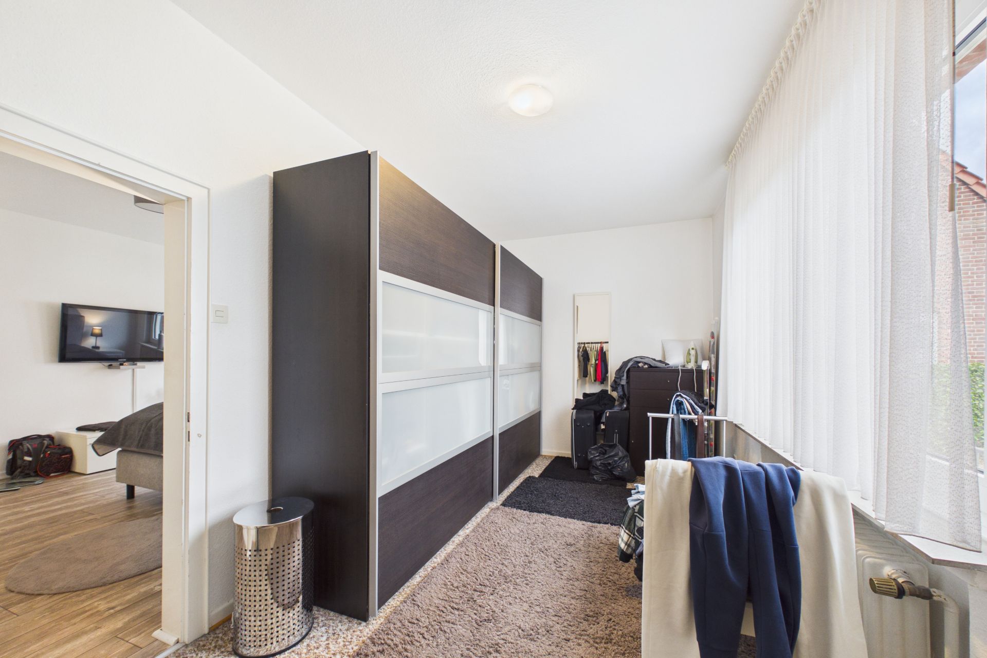 Heller Raum mit großem Schrank, Teppichboden und Kleiderständer am Fenster.