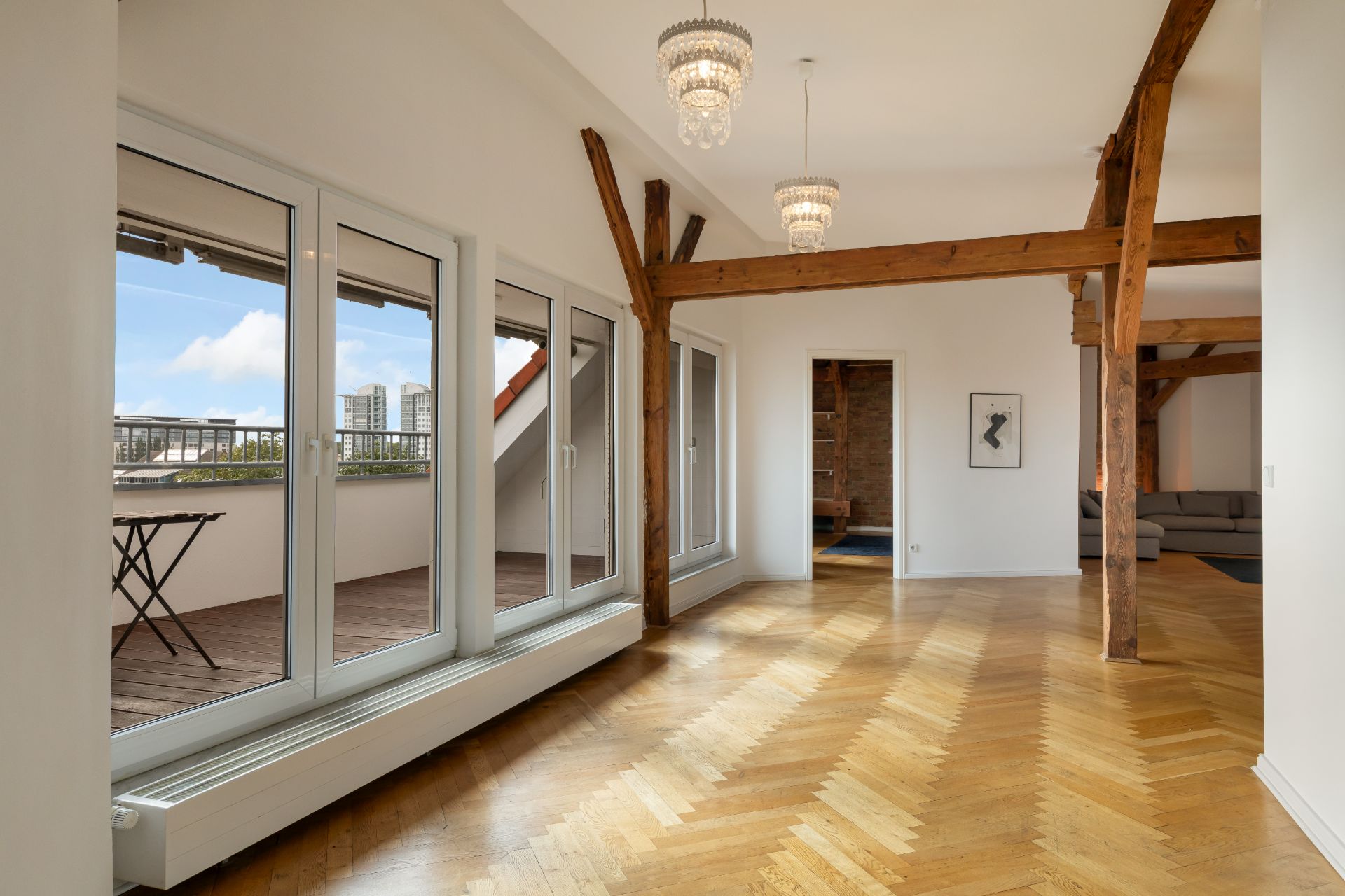 Heller Wohnraum mit Holzfußboden, Holzbalken, Kronleuchtern und Zugang zu einem Balkon.