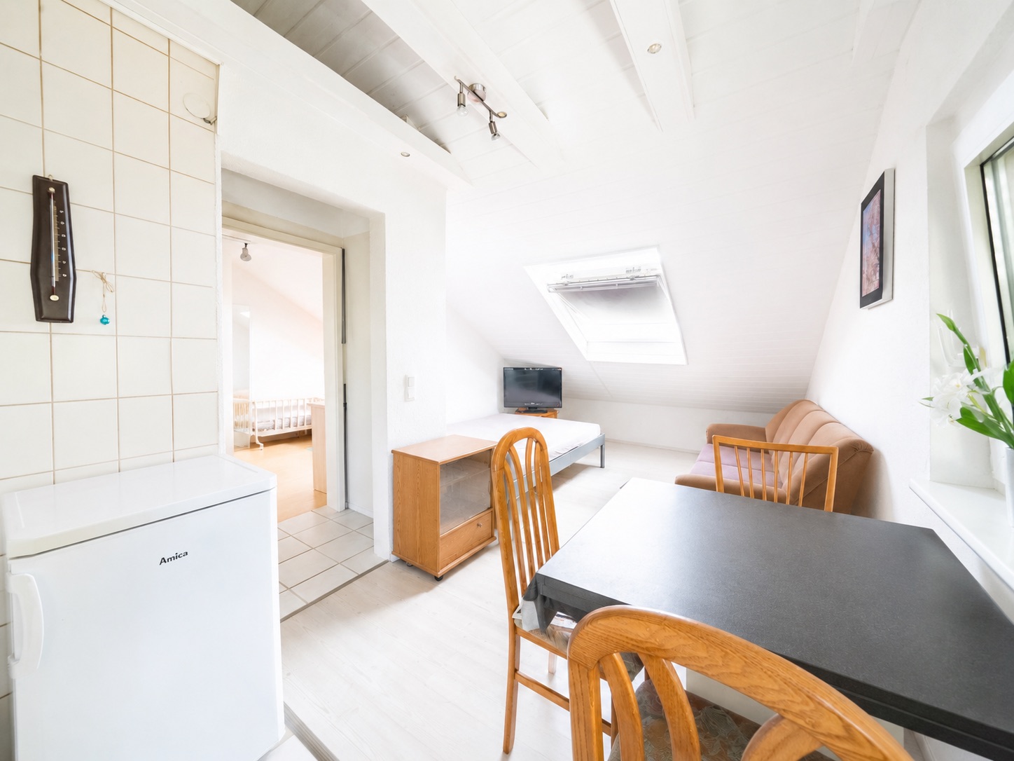 Helles Wohnzimmer mit Sofa, Esstisch, Stühlen, Fernseher und Dachfenster.
