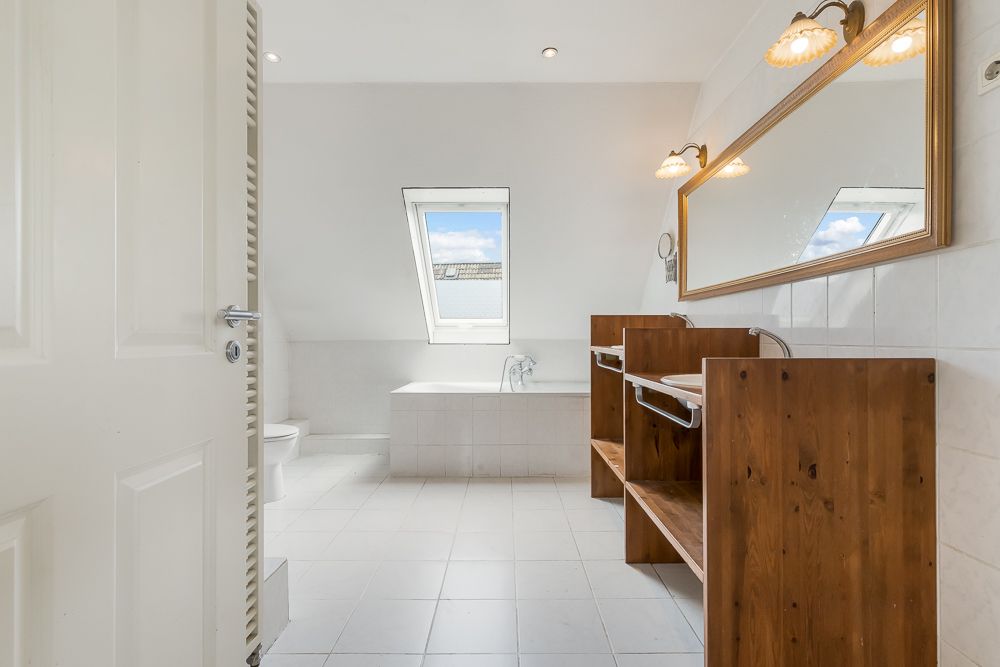 Helles Badezimmer mit Badewanne, großem Spiegel und Holzwaschtischen unter einem Dachfenster.