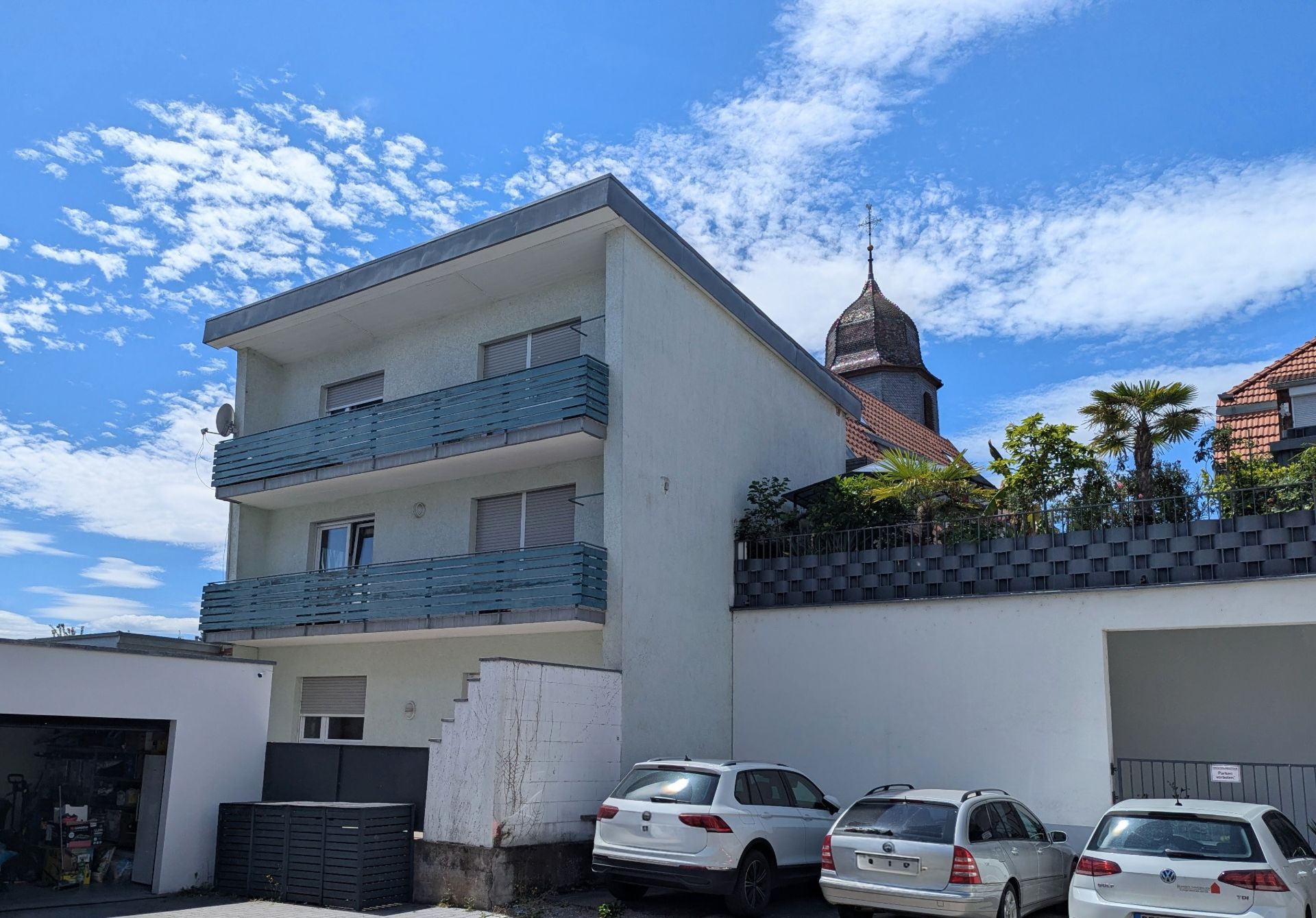 Modernes, dreistöckiges Wohnhaus mit blauen Balkonen und parkenden Autos davor.