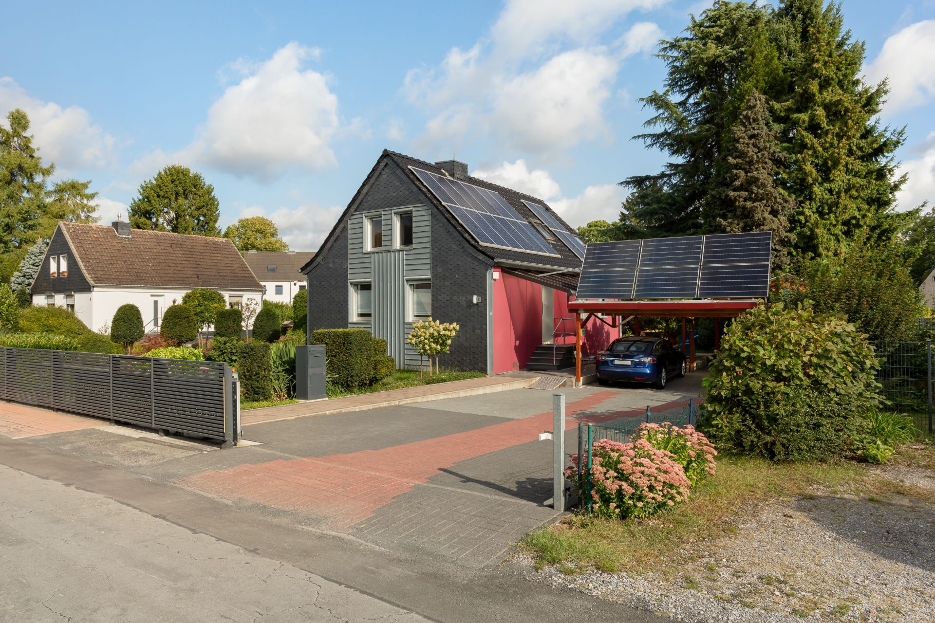 Modernes Wohnhaus mit Carport und Solaranlagen auf Dach und Carport, umgeben von Garten und Einfahrt.