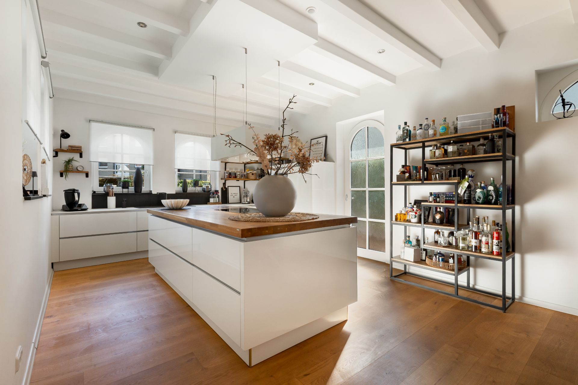 Helle, moderne Küche mit Kücheninsel, Holzfußboden und Regal mit Flaschen an der Wand.