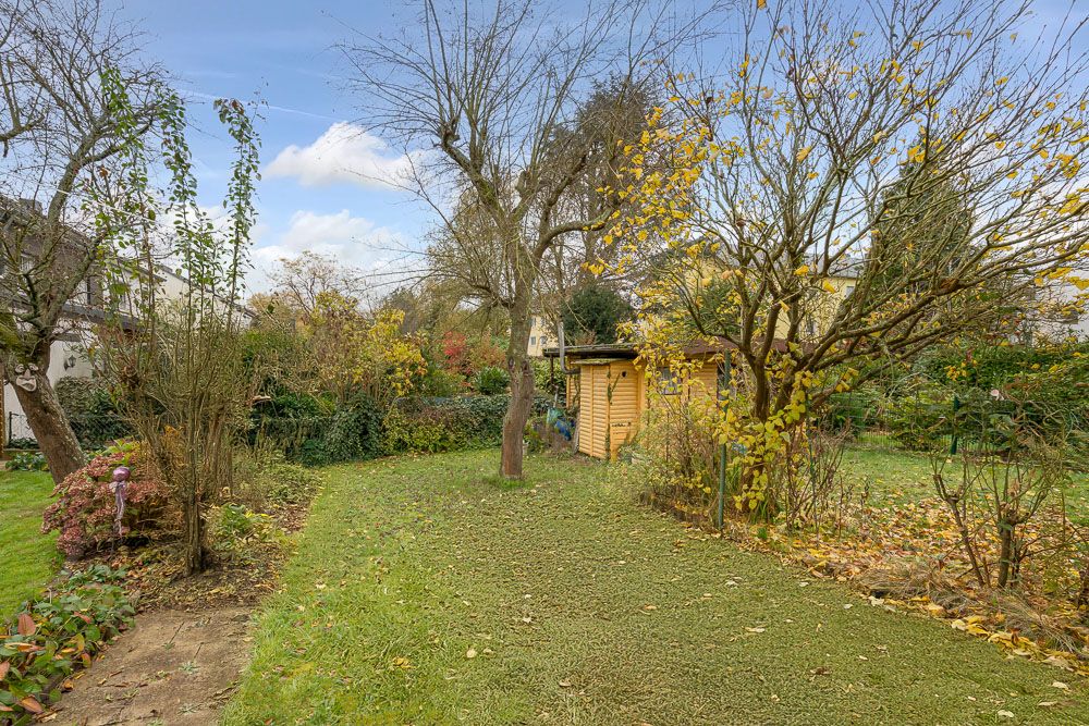 Garten mit Rasen, Bäumen, Sträuchern und einem kleinen Holzhaus im Hintergrund.