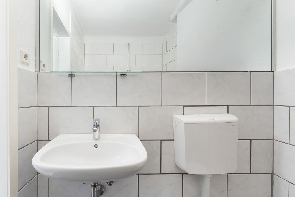Kleines Badezimmer mit Fliesen, Waschbecken, Spiegel und Toilettenspülkasten.