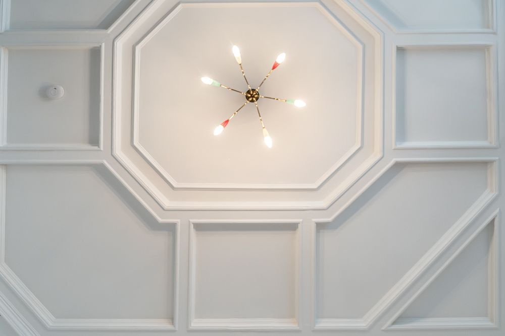 Weiße Decke mit achteckigem Muster und moderner Deckenleuchte mit sechs Glühbirnen.