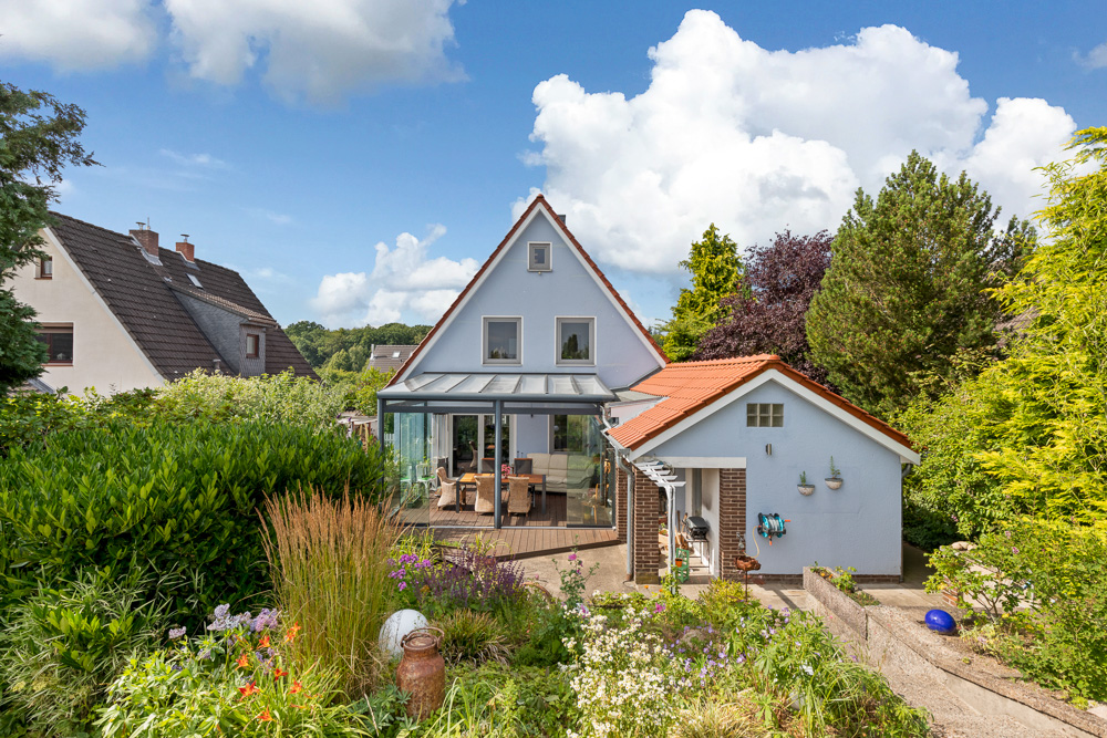 Einfamilienhaus mit Wintergarten, Nebengebäude und gepflegtem Garten bei Tageslicht.