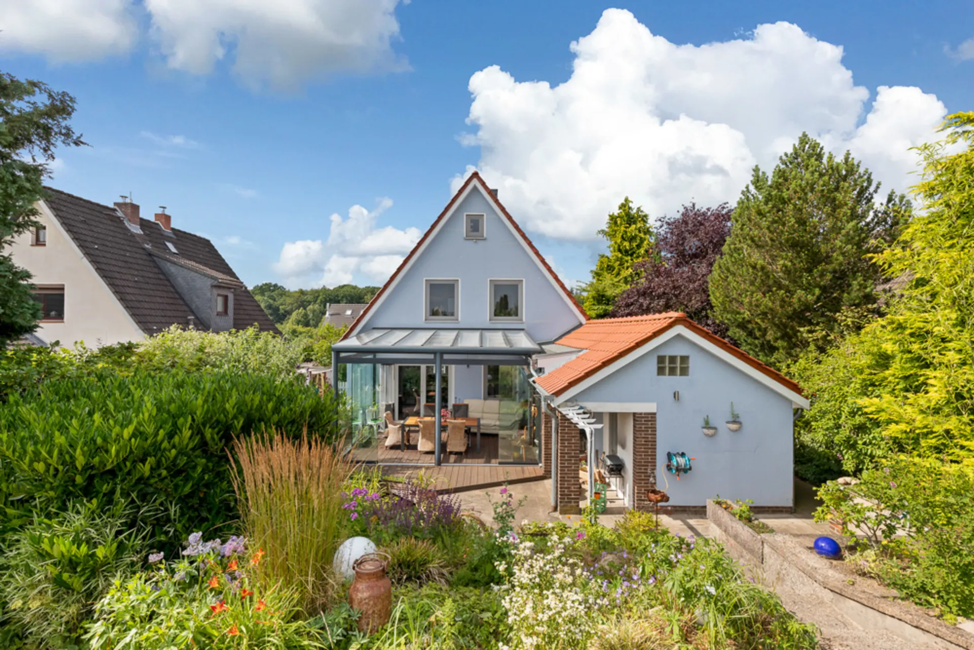 Einfamilienhaus mit Wintergarten, Nebengebäude und gepflegtem Garten bei Tageslicht.