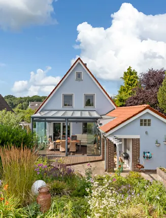 Einfamilienhaus mit Wintergarten, Nebengebäude und gepflegtem Garten bei Tageslicht.