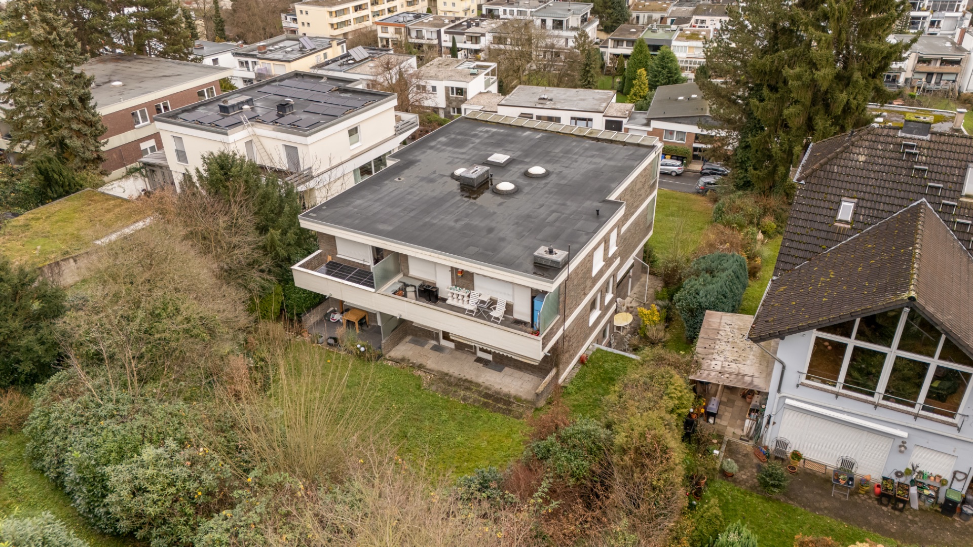 Mehrfamilienhaus mit Flachdach, Balkonen und Garten, von oben fotografiert.