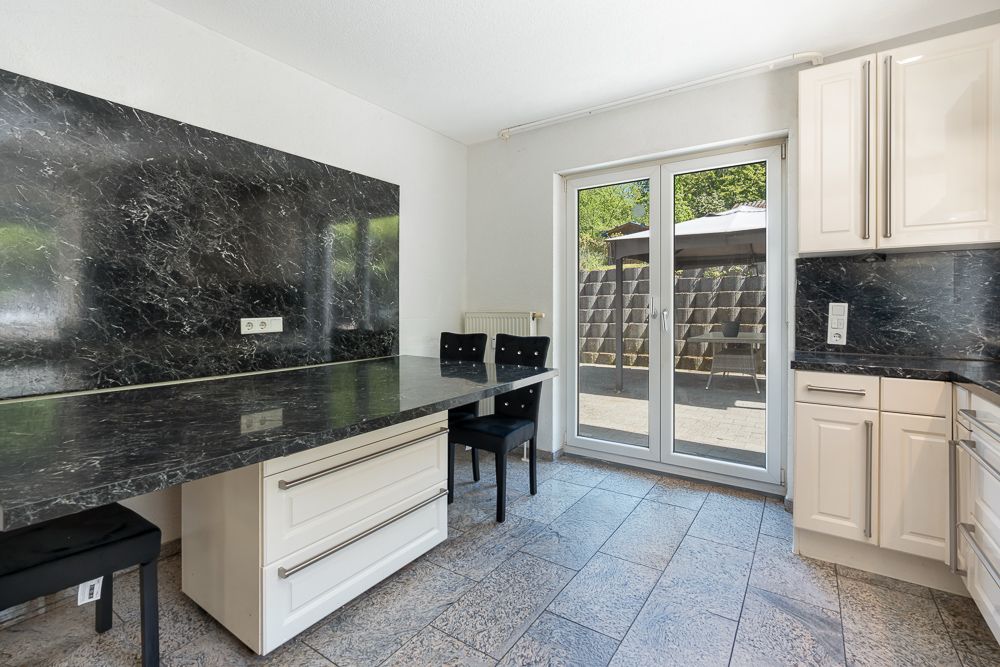 Moderne Küche mit schwarzer Marmorarbeitsplatte und Esstisch, zwei Stühlen und Zugang zur Terrasse.