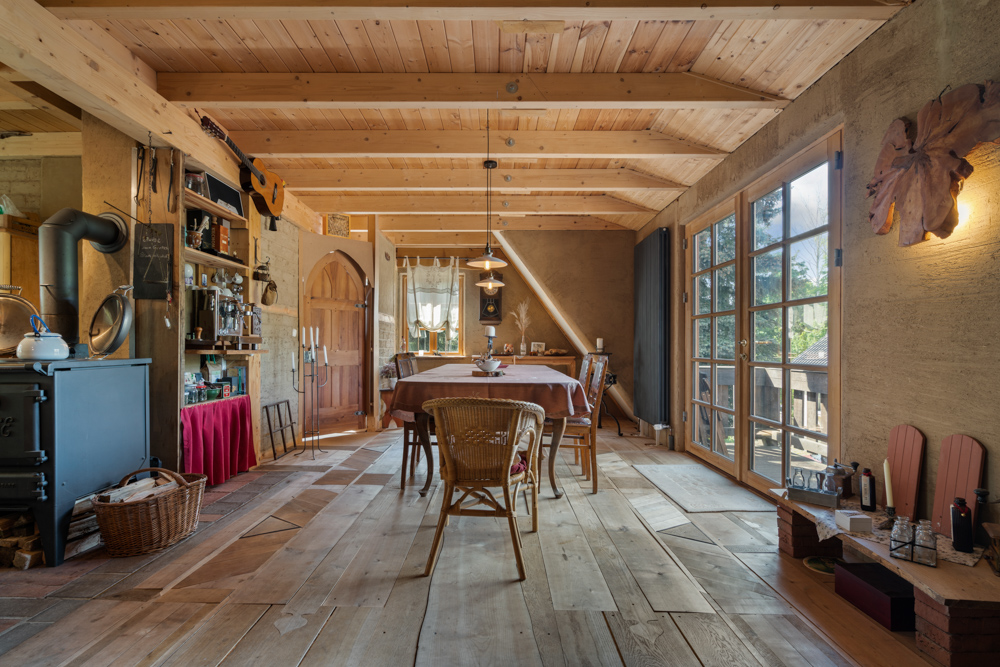 Gemütliches Esszimmer mit Holzboden, Kamin, großen Fenstern und einem gedeckten Tisch.