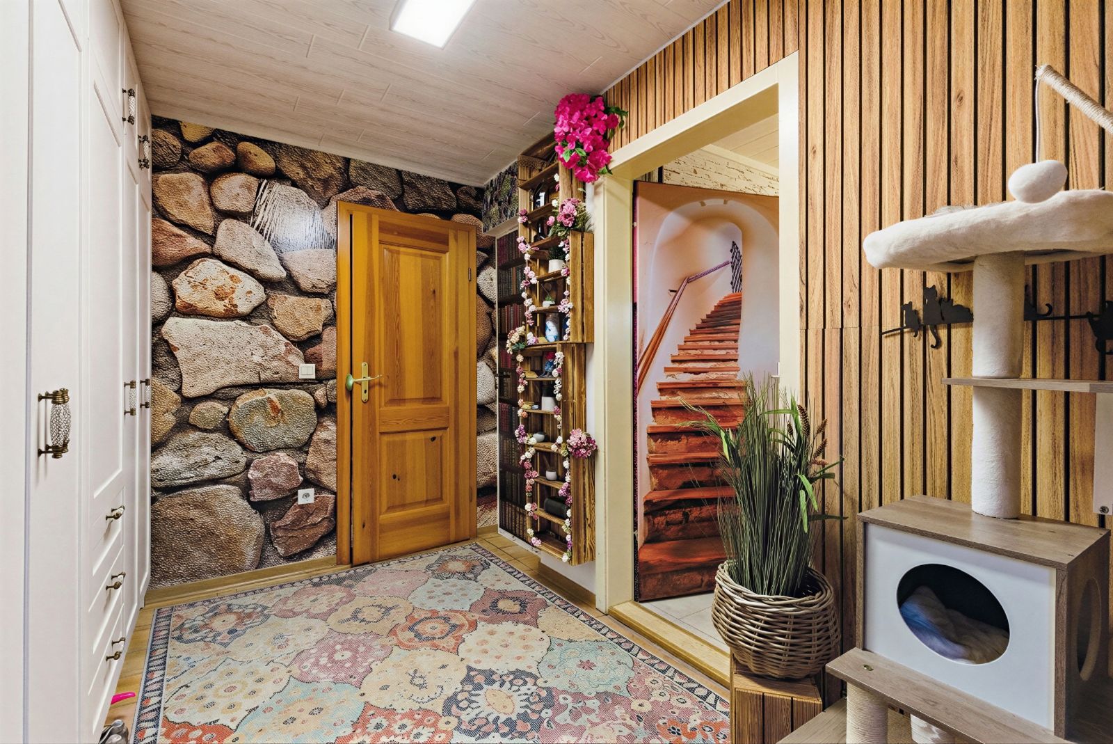 Flur mit gemusterem Teppich, Holztür, Pflanzen, Kratzbaum und Treppe im Hintergrund.