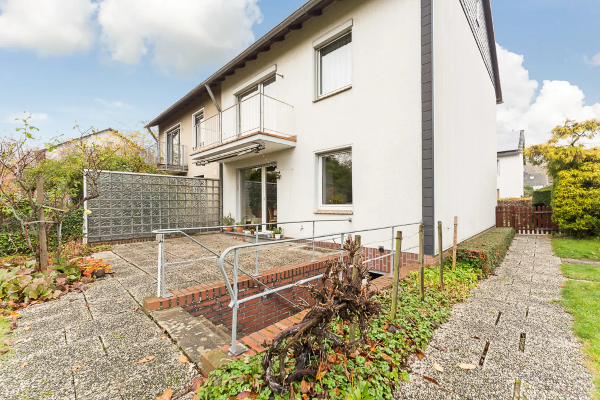 Zweistöckiges Haus mit Terrasse, Rampe, Geländer und Gartenweg aus Pflastersteinen.