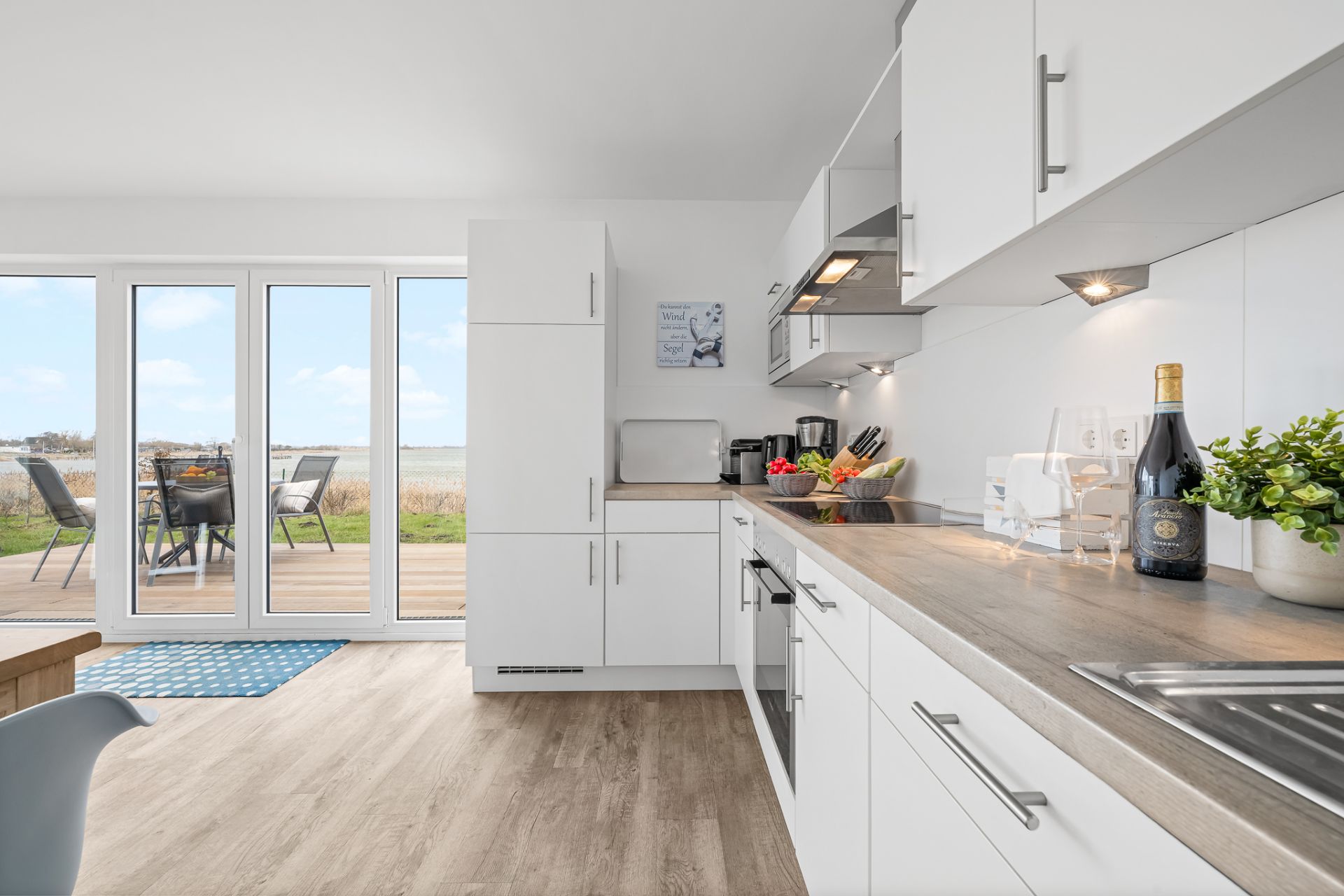 Moderne, helle Einbauküche mit Blick auf Terrasse und Garten durch große Glastüren.