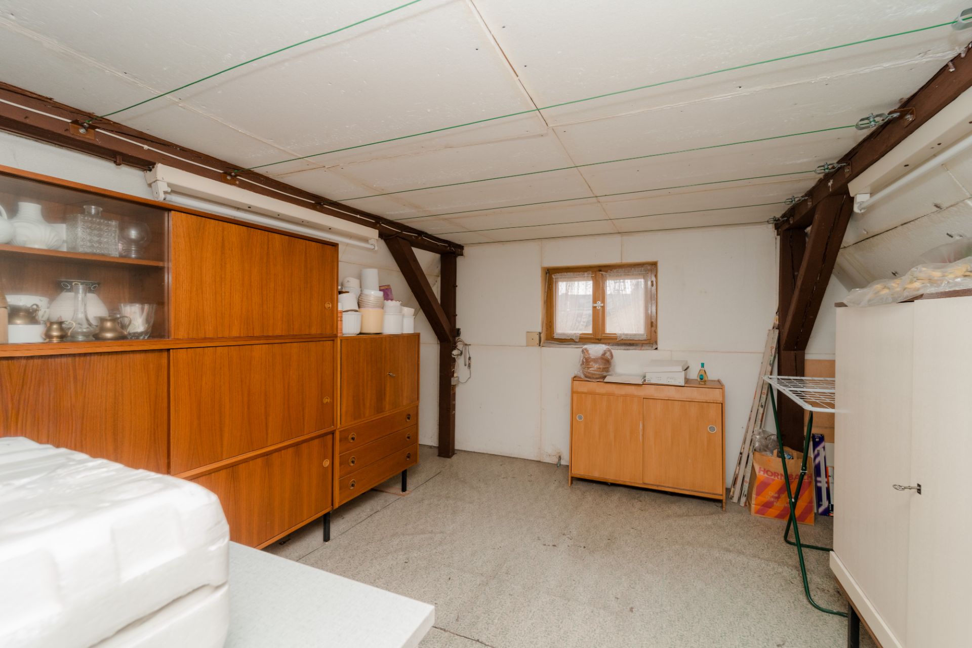 Kellerraum mit Holzschränken, kleinem Fenster und Haushaltsgegenständen.
