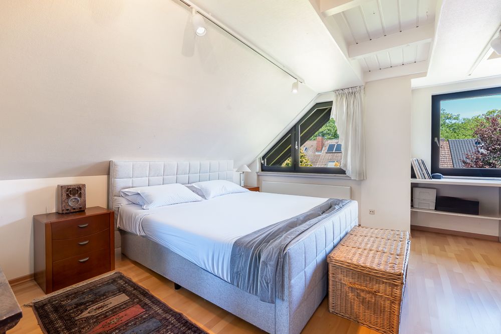 Helles Schlafzimmer mit Doppelbett, Nachttisch, Fenster und Korb auf Holzfußboden.