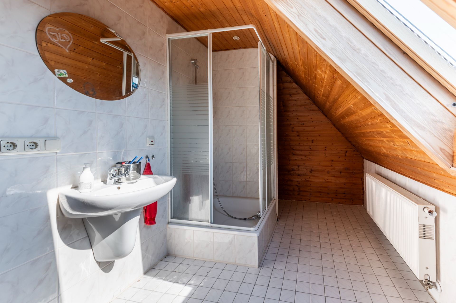 Dachbad mit Waschbecken, Spiegel, Dusche und Dachschräge mit Holzverkleidung.