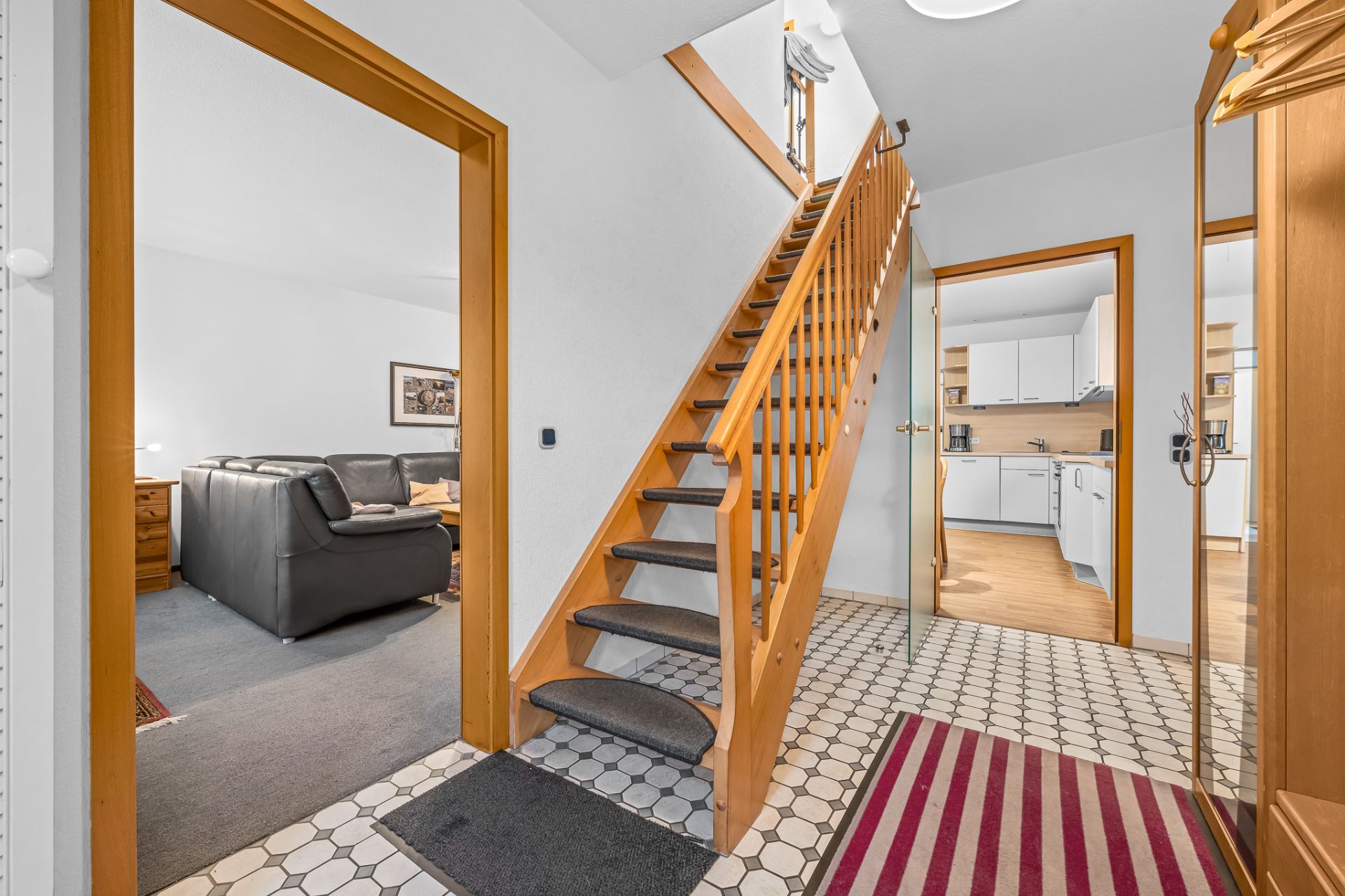 Flur mit Holztreppe, Blick ins Wohnzimmer links und Küche rechts.
