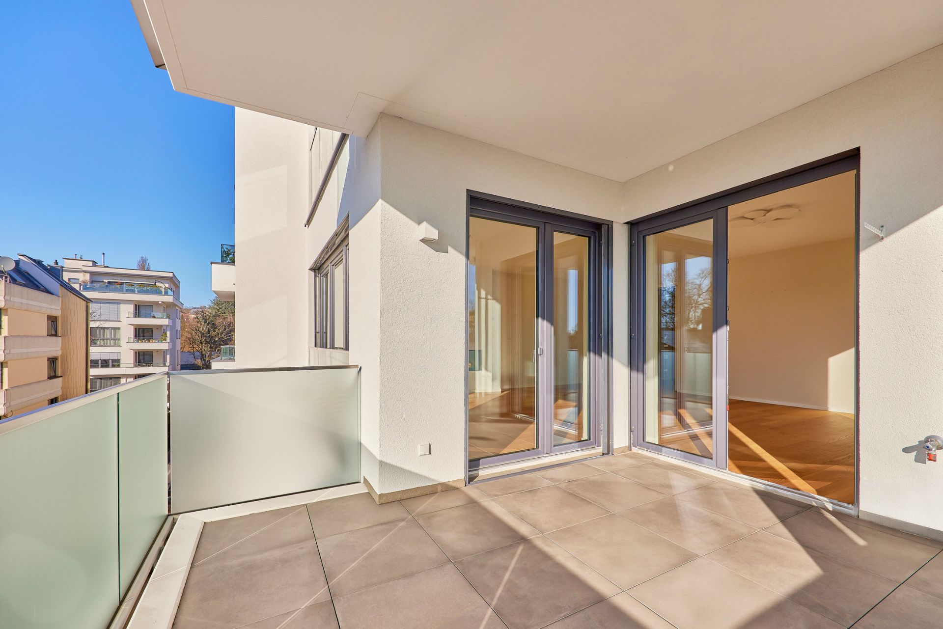 Moderne Loggia mit Glasgeländer und Zugang zu einem hellen Wohnraum durch große Fenstertüren.