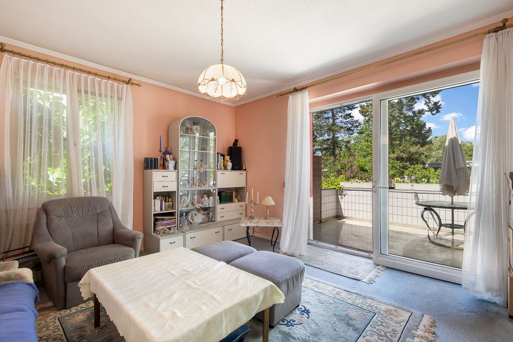 Helles Wohnzimmer mit Sessel, Vitrine, Couchtisch und Zugang zur Terrasse mit Sitzplatz.