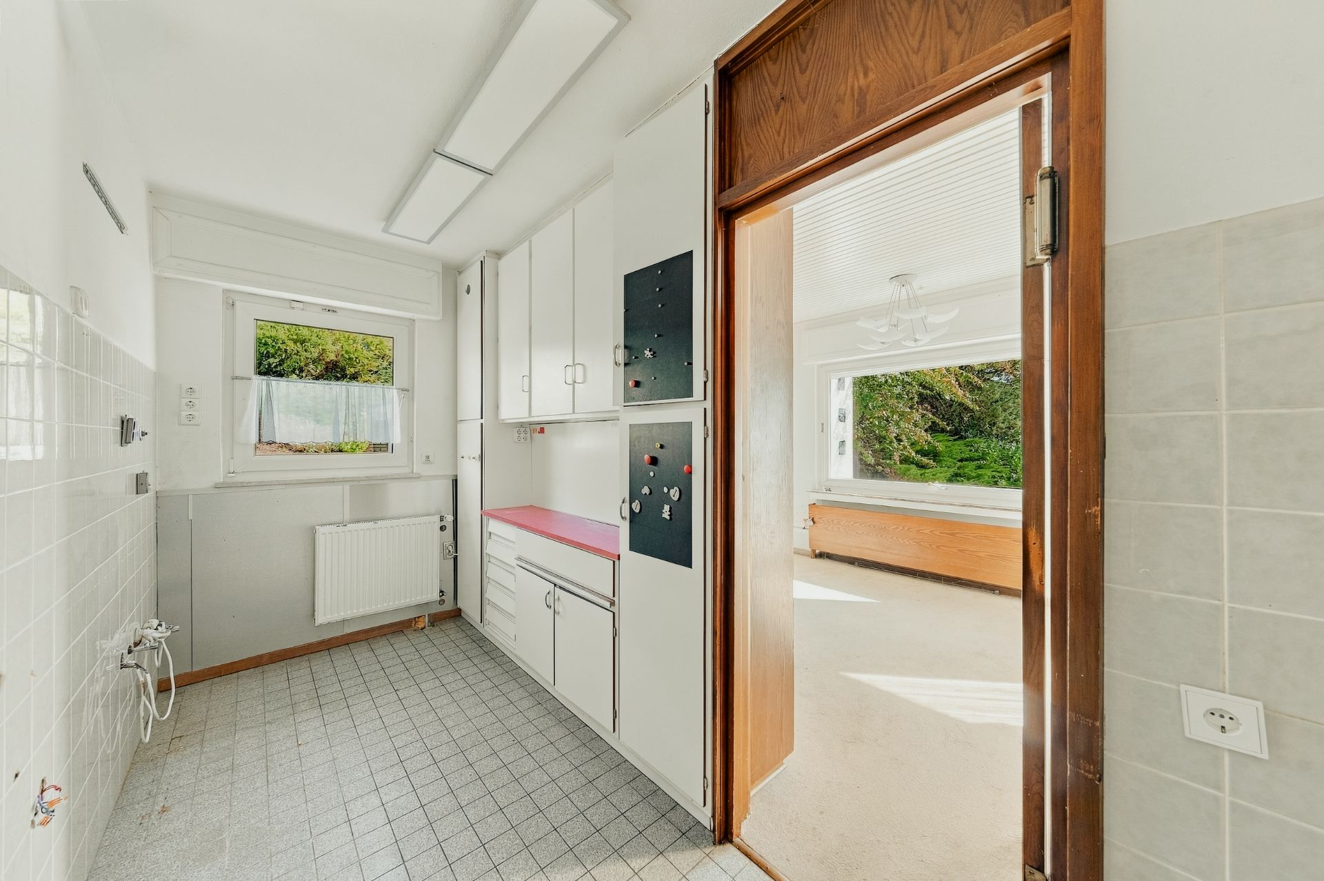 Helle Küche mit weißen Schränken, roter Arbeitsplatte und Blick ins angrenzende Wohnzimmer.