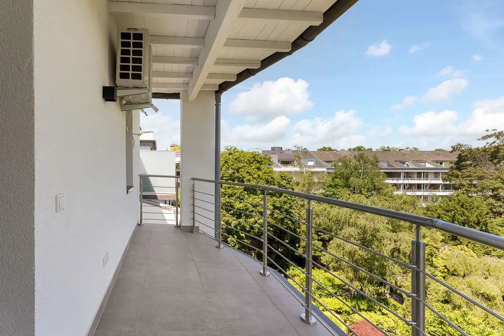 Überdachter Balkon mit Metallgeländer, Blick auf Bäume und benachbarte Wohnhäuser.