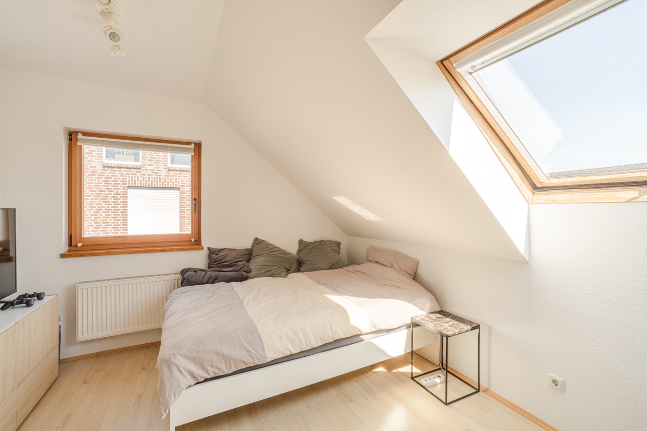 Helles Schlafzimmer mit Doppelbett, Dachschräge, Fenster und Nachttisch.