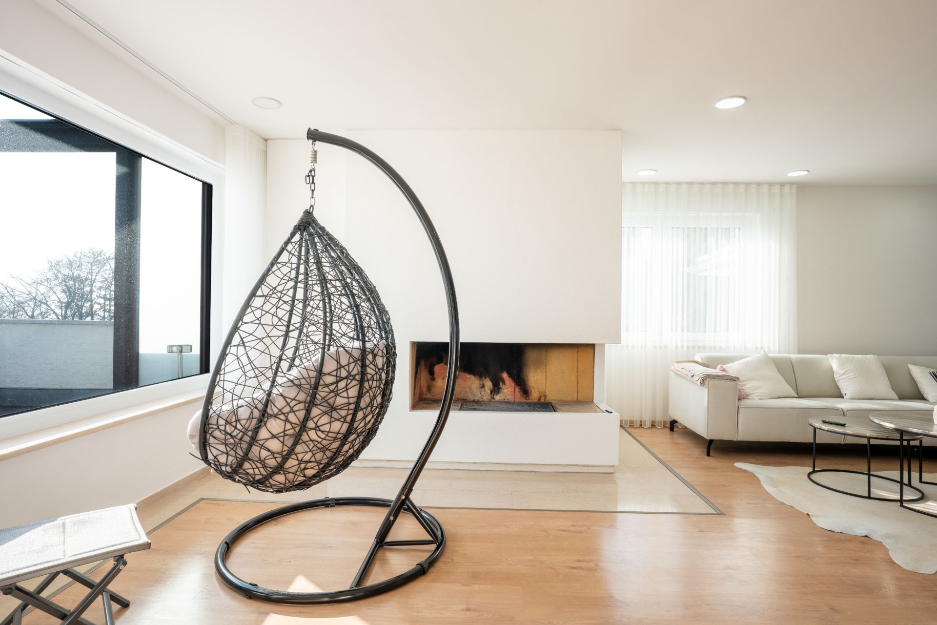 Modernes Wohnzimmer mit Hängesessel, Kamin, großem Fenster und weißem Sofa.
