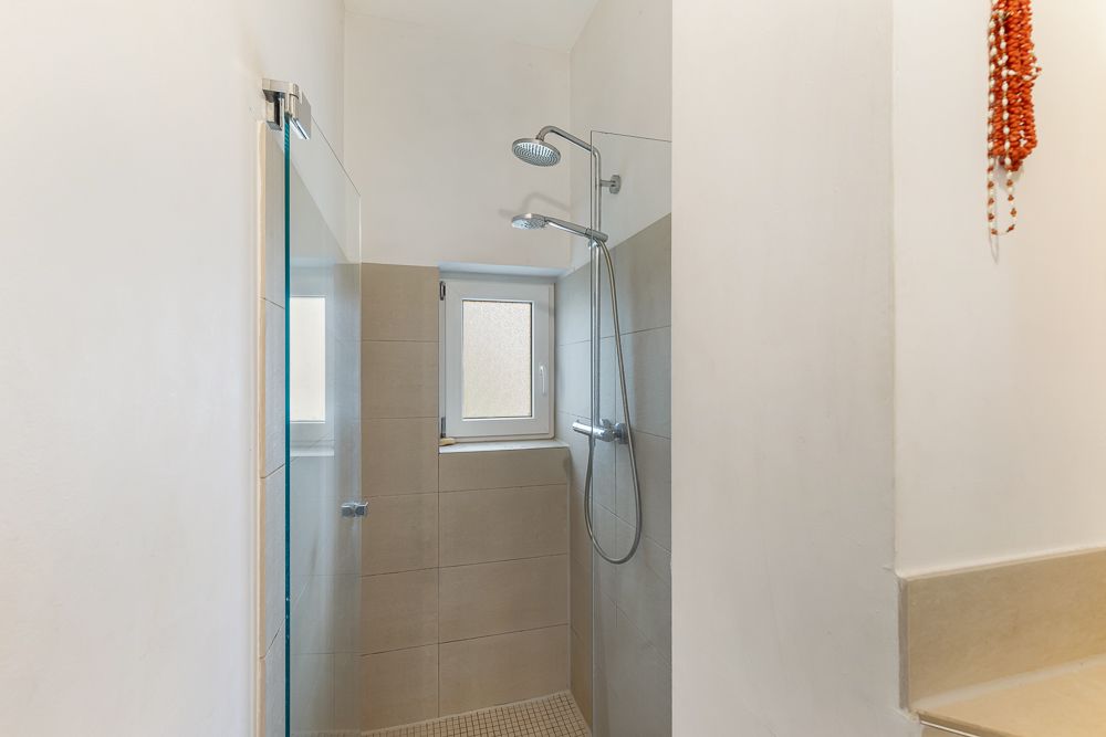 Moderne, offene Dusche mit zwei Duschköpfen und kleinem Fenster in einem hellen Badezimmer.