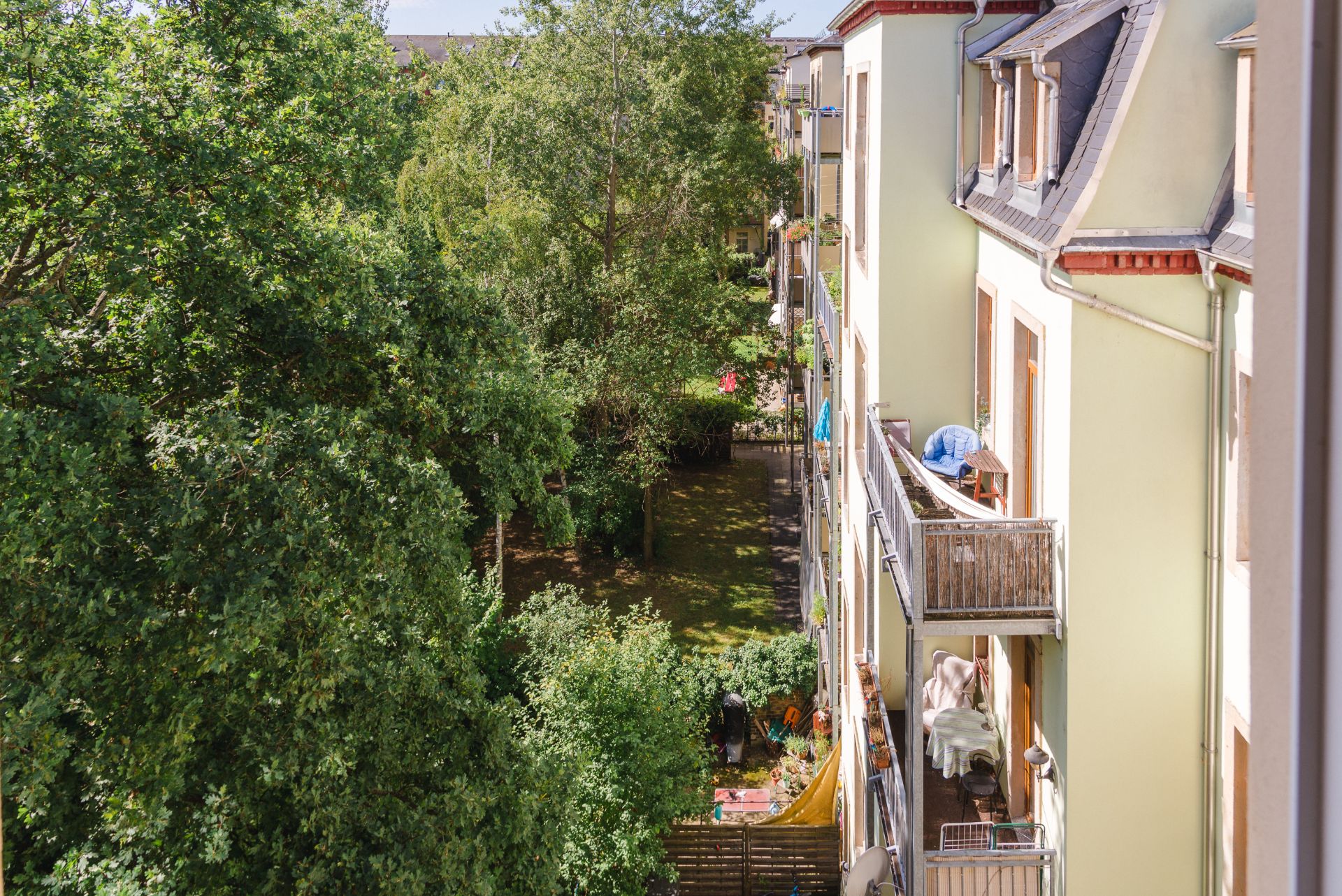 Blick auf einen begrünten Innenhof mit Bäumen und Balkonen eines Wohnhauses.