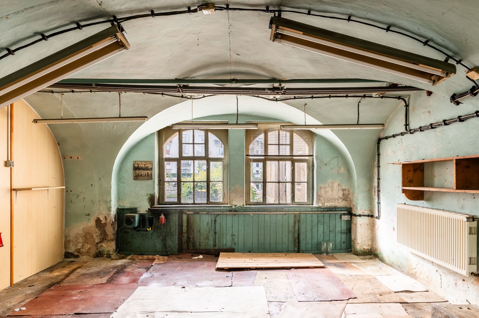 Alter, leerer Raum mit gewölbter Decke, großen Fenstern und sichtbaren Gebrauchsspuren.