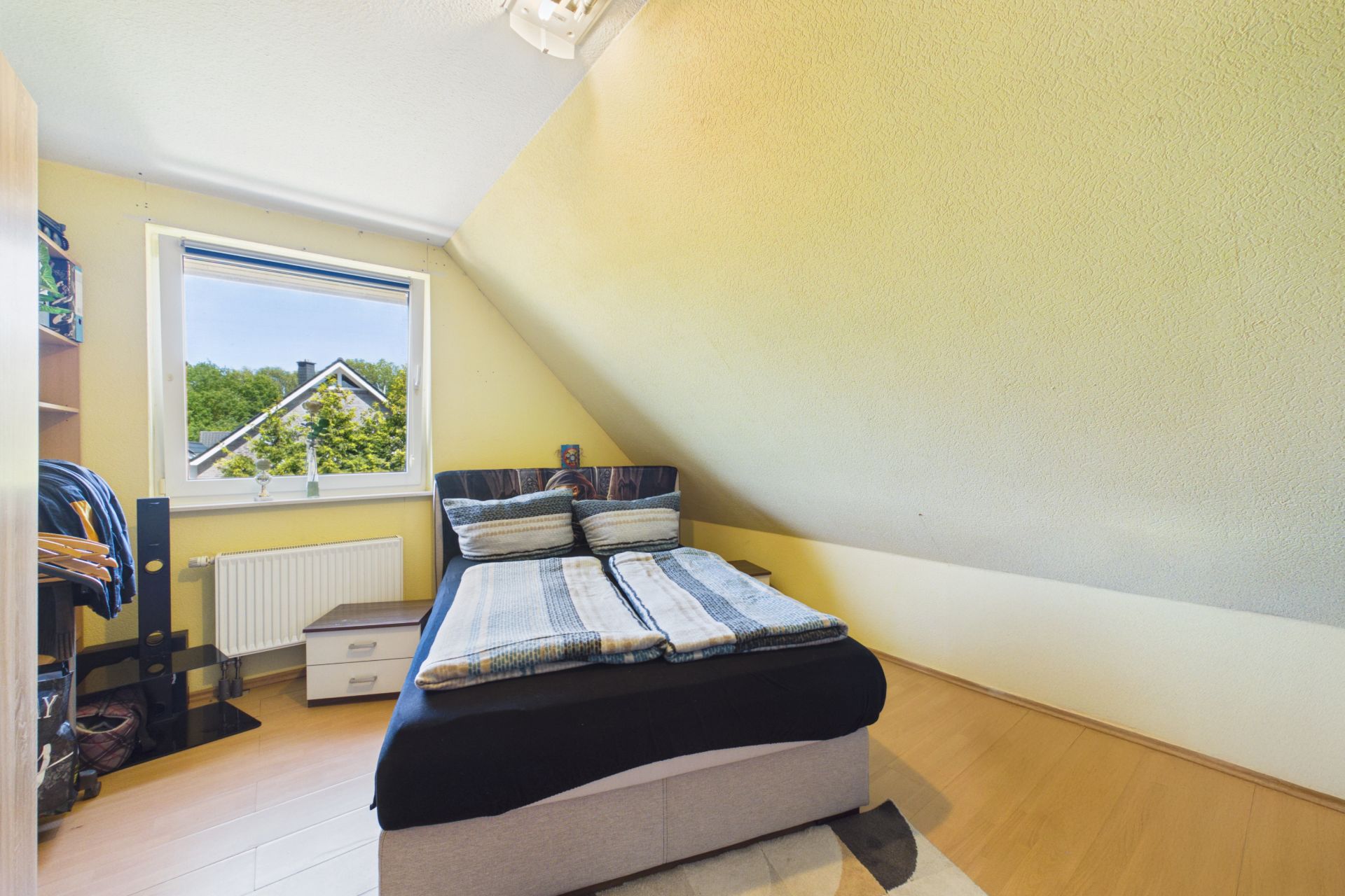Schlafzimmer mit Doppelbett unter Dachschräge, Fenster mit Ausblick, heller Holzboden.