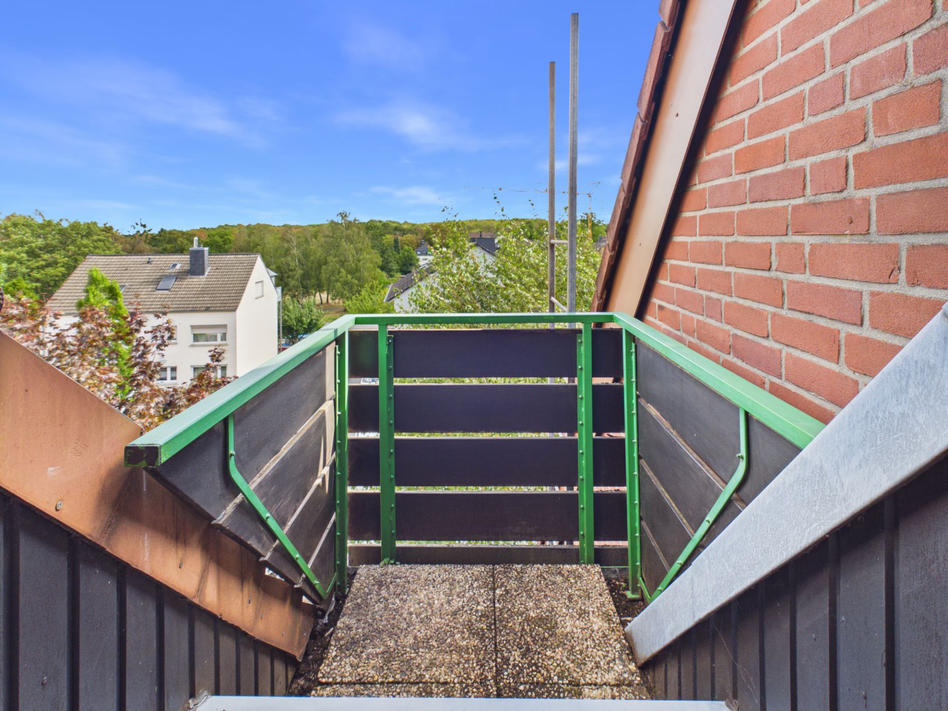 Kleiner Balkon mit Blick auf Nachbarhäuser und viel Grün im Hintergrund.