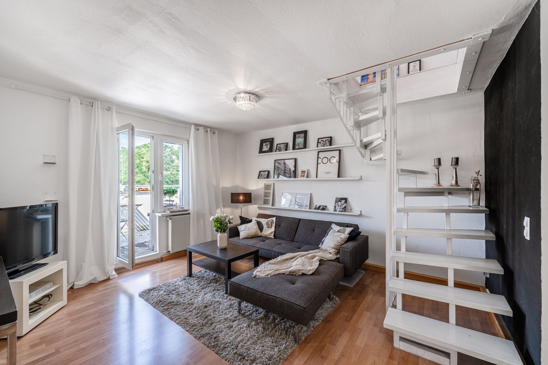 Modernes Wohnzimmer mit Sofa, Couchtisch, Teppich, Treppe und Balkonzugang.