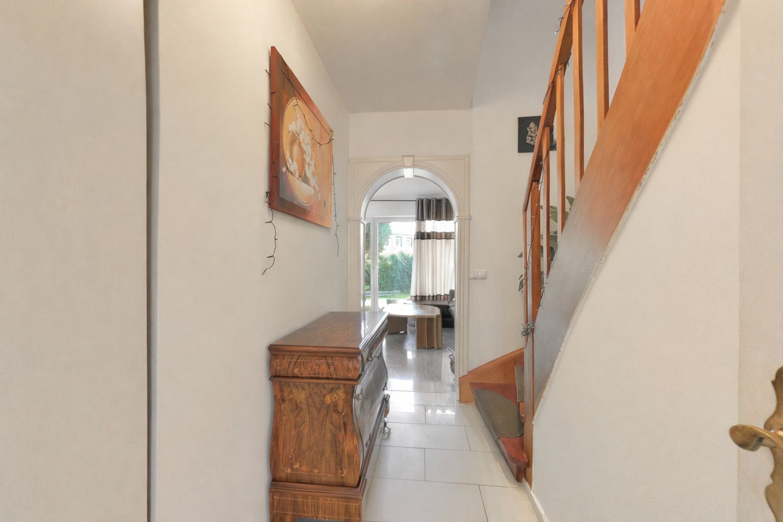Heller Flur mit Holztreppe, Kommode und Gemälde, Blick Richtung Wohnraum.
