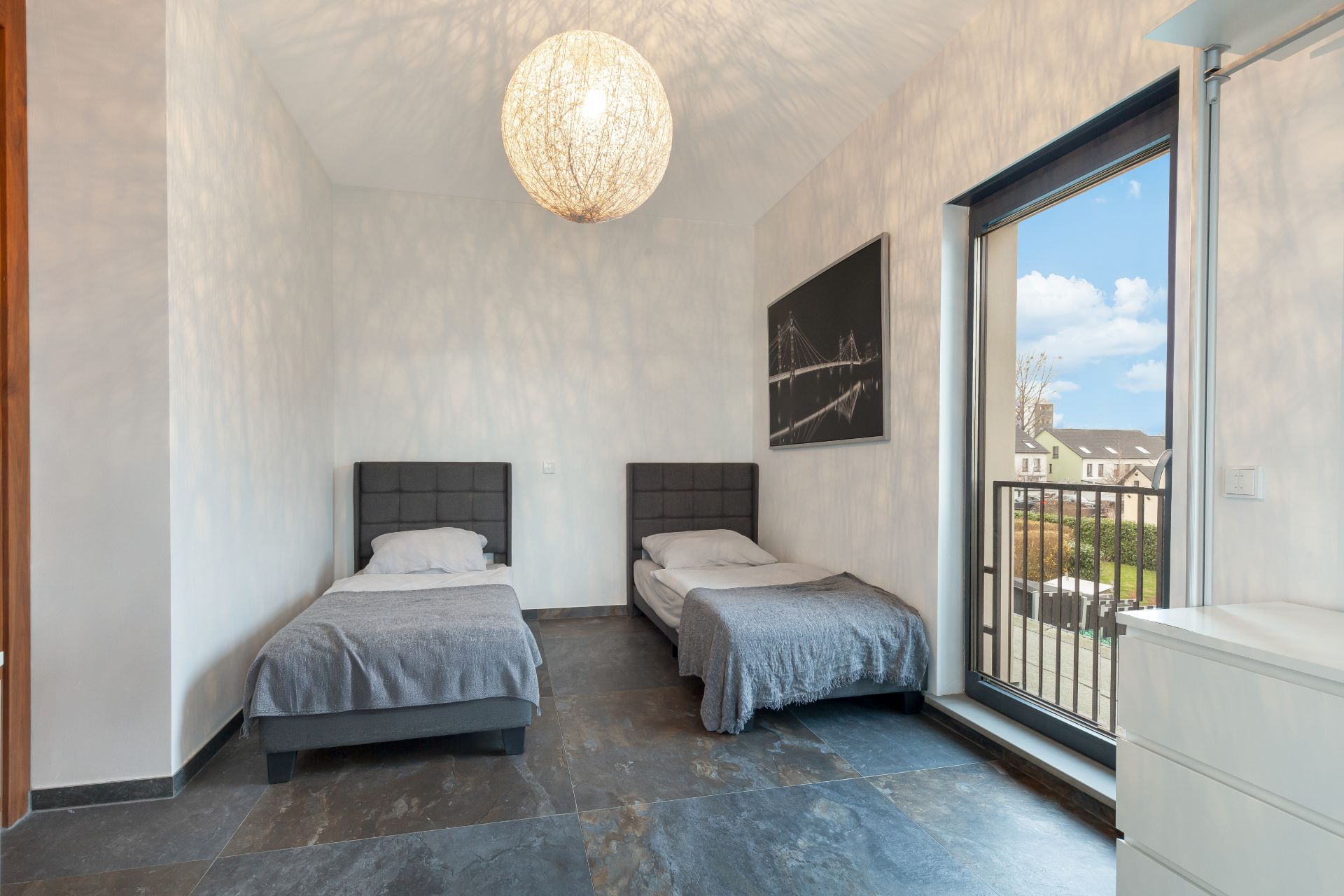 Schlafzimmer mit zwei Einzelbetten, großem Fenster und moderner Hängelampe.