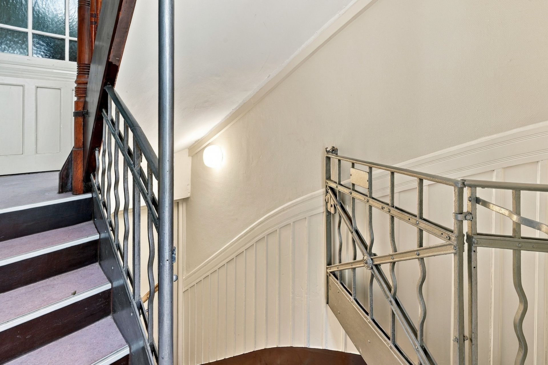 Helles Treppenhaus mit Metallgeländer und Holzelementen in einem Wohnhaus.