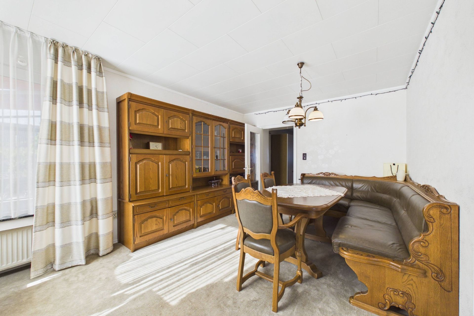 Esszimmer mit Holzeckbank, Tisch, Stühlen und großem Holzschrank an der Wand.