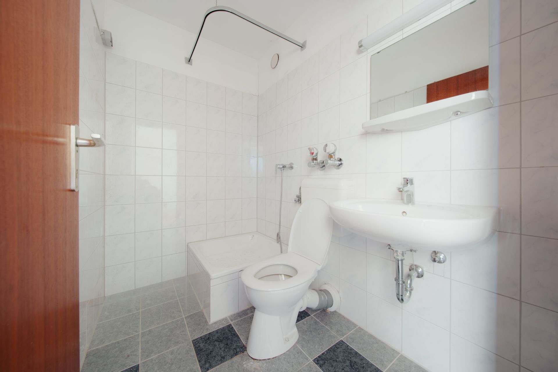 Helles Badezimmer mit WC, Waschbecken, Spiegel und kleiner Badewanne auf gefliestem Boden.